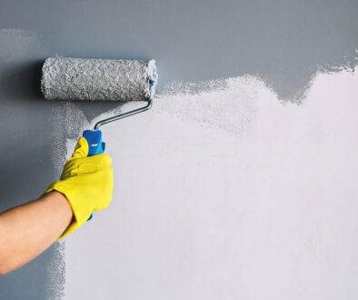 Hand in yellow glove painting wall in gray color with a roller brush.